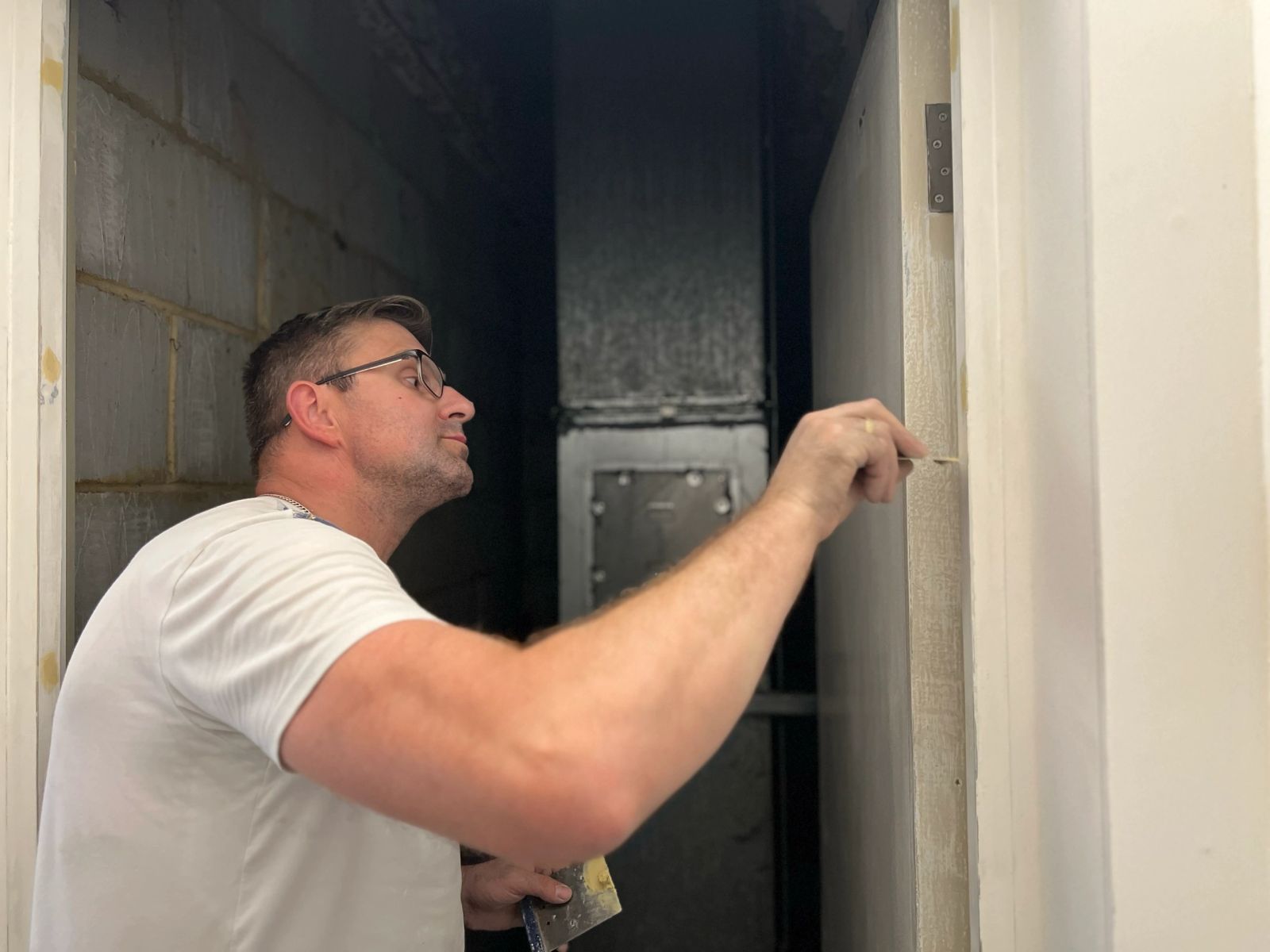 A man wearing glasses and a white shirt is painting a wall.